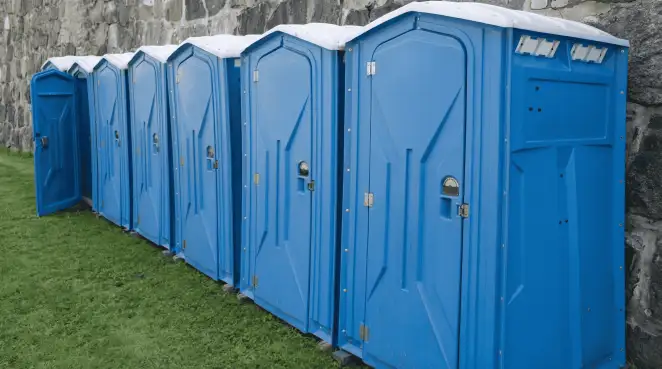 Row of blue portable toilets lined up on grass against a stone wall for event sanitation in Boise, ID