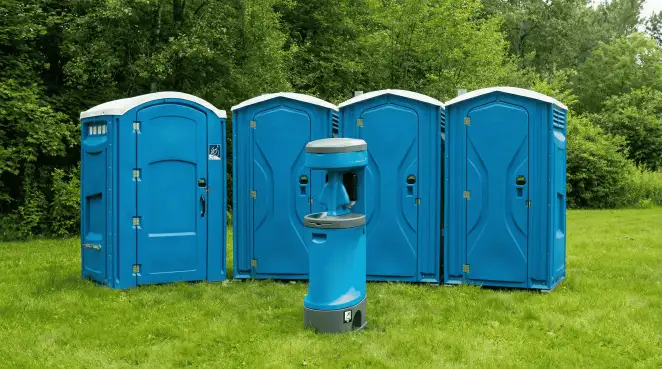 Four blue portable toilets and a matching hand washing station on grass near trees, a common sight at local outdoor events in Boise, ID