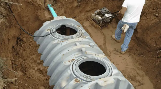 Septic tank installation showing a technician compacting soil around a new poly septic tank in an excavation pit in Boise, ID